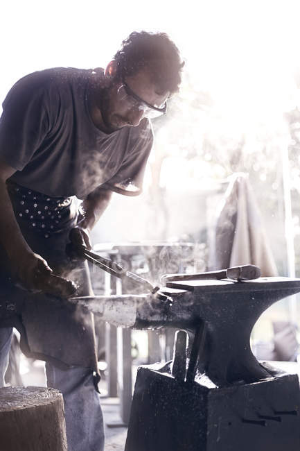 Blacksmith shaping iron over anvil in forge — Stock Photo