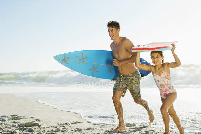 Отец и дочь несут доску для серфинга и бодиборд на пляже — стоковое фото