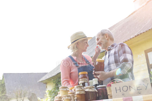 Casal sênior afetuoso vendendo mel no mercado de agricultores — Fotografia de Stock