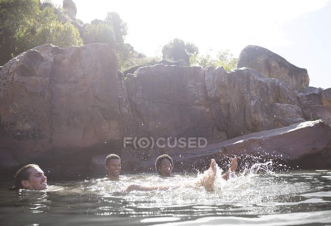 Amigos jugando en el río contra el rock - foto de stock