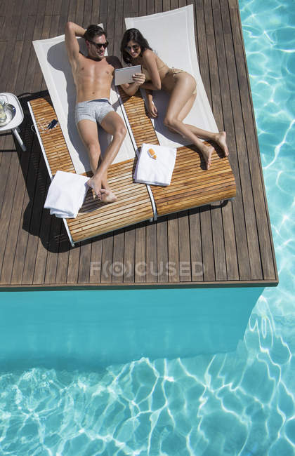 Пара отдыха на шезлонгах у бассейна с ноутбуком — стоковое фото