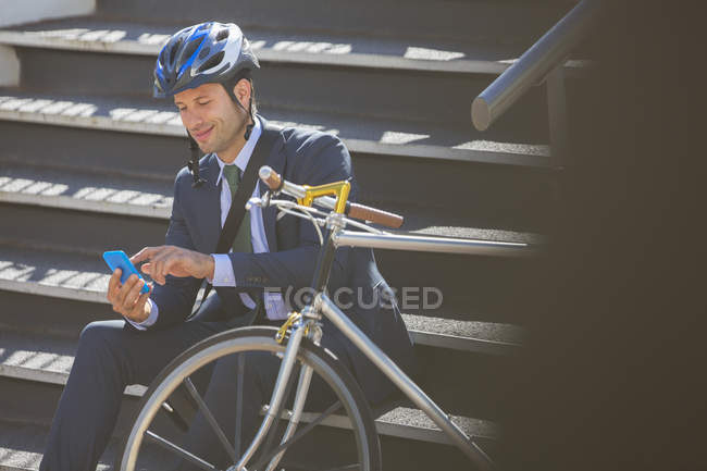 Empresario en traje con bicicleta y mensajes de texto casco con teléfono celular en las escaleras - foto de stock