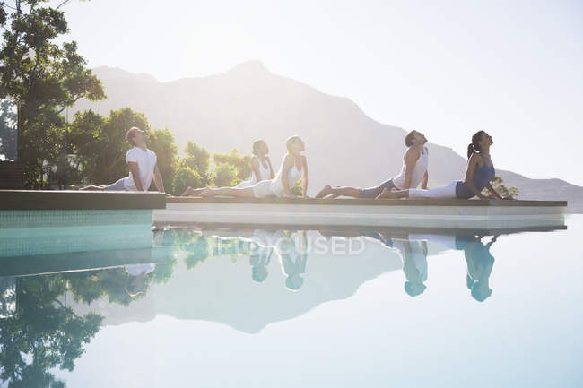 Jeunes gens attrayants pratiquant le yoga au bord de la piscine — Photo de stock