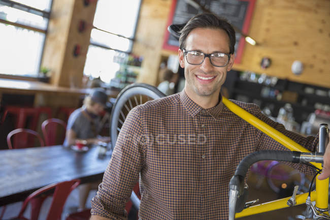 Portrait smiling man with eyeglasses carrying bicycle in cafe — Stock Photo