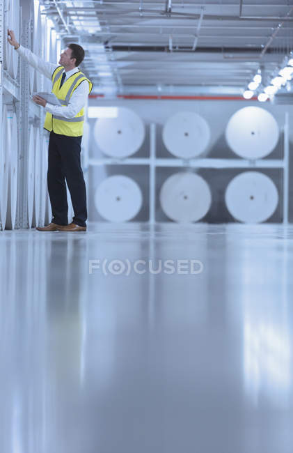 Trabajador examinando grandes bobinas de papel en la planta de impresión - foto de stock