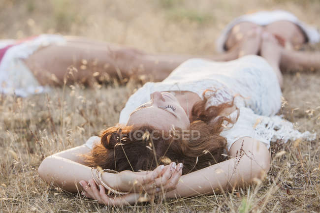 Boho women laying in circle with feet touching in rural field — Stock Photo
