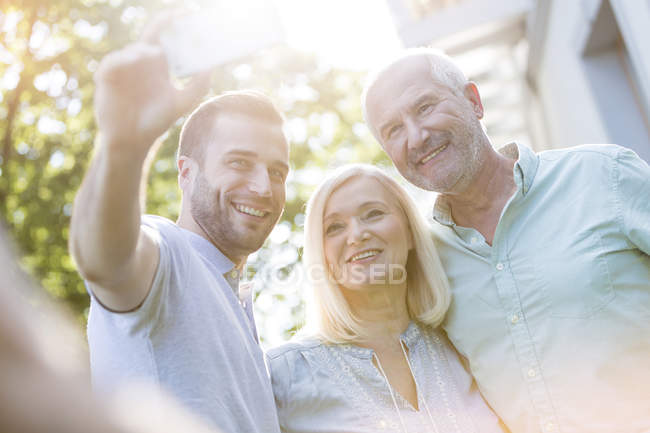 Усміхнена старша пара і дорослий син бере селфі на відкритому повітрі — стокове фото