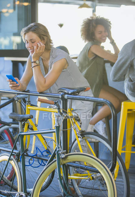 Smiling woman leaning on railing texting with cell phone above bicycle — Stock Photo