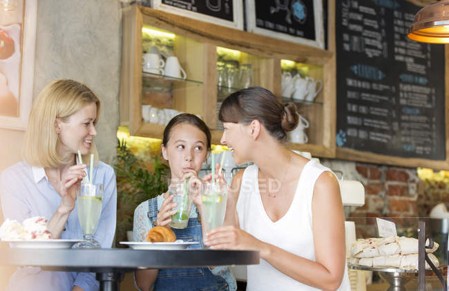 Dos mujeres y una niña tomando cócteles en la cafetería - foto de stock