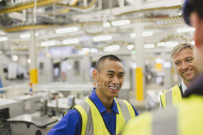 Рабочие в отражающей одежде разговаривают на фабрике — стоковое фото