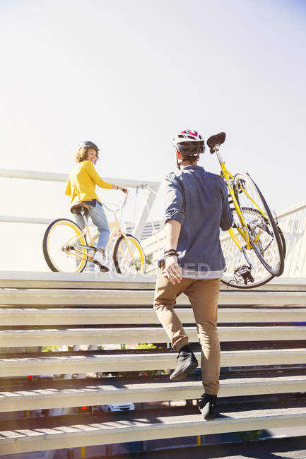 Hombre en casco llevando bicicleta escaleras urbanas - foto de stock