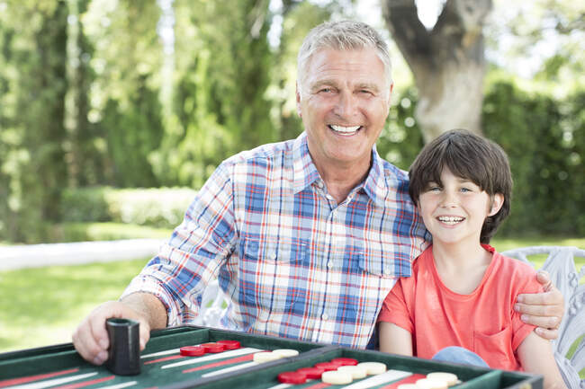 Abuelo y nieto jugando backgammon en el patio - foto de stock