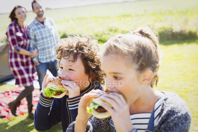 Brother and sister eating hamburgers at sunny campsite — Stock Photo