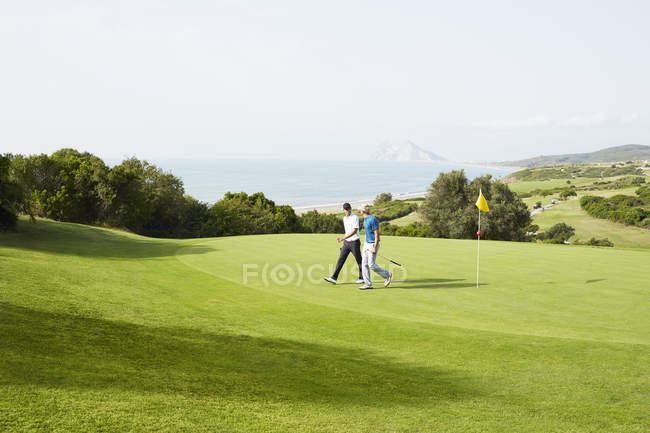 Homens caminhando no campo de golfe com vista para o oceano — Fotografia de Stock