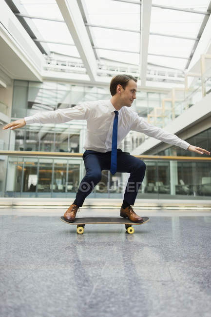 Juguetón hombre de negocios skateboarding en pasillo de oficina - foto de stock