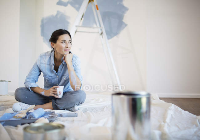 Woman relaxing with coffee among painting supplies — Stock Photo