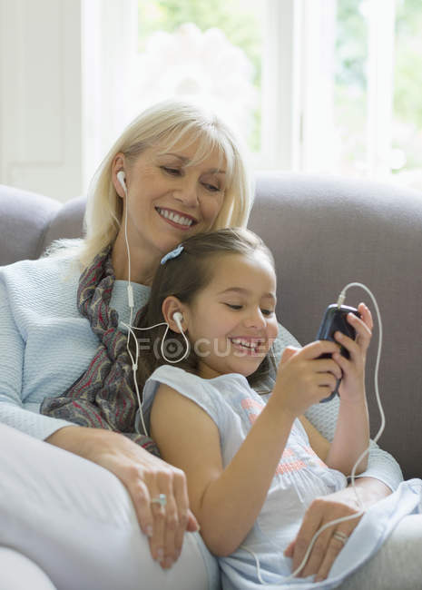 Бабуся і онука діляться навушниками, слухаючи музику на дивані — стокове фото