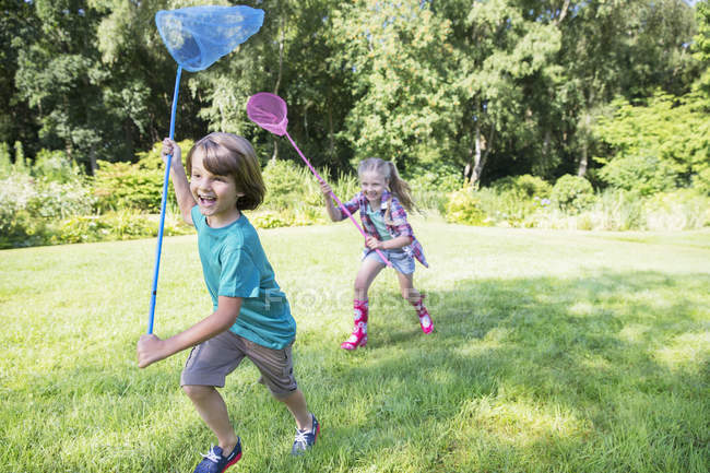 Menino e menina correndo com redes de borboleta na grama — Fotografia de Stock