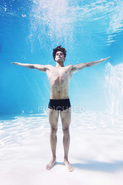 Hombre parado bajo el agua en la piscina con los brazos extendidos - foto de stock