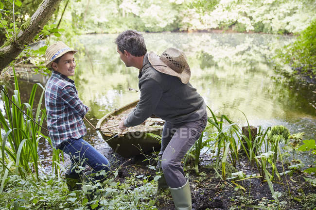 Padre e hijo tirando del barco a la orilla en el estanque - foto de stock