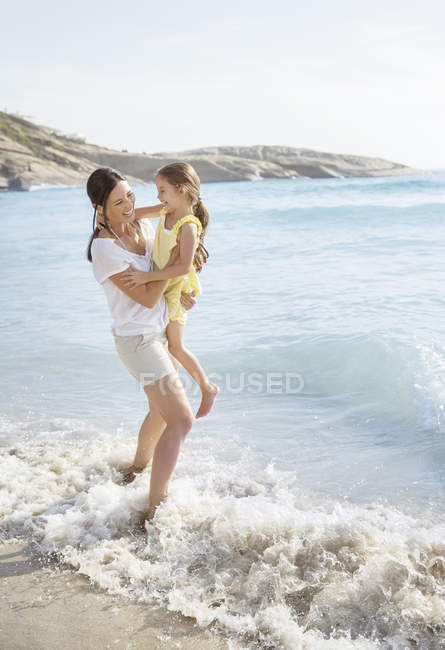 Mãe e filha brincando em ondas na praia — Fotografia de Stock