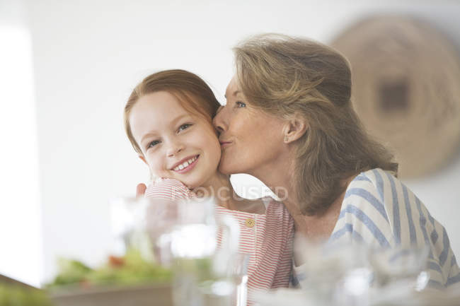 Літня жінка цілує онуку за столом — стокове фото