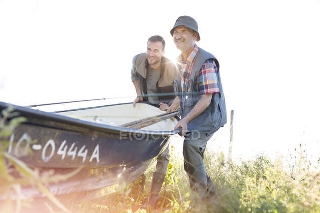 Padre e hijo adulto levantando barco de pesca - foto de stock