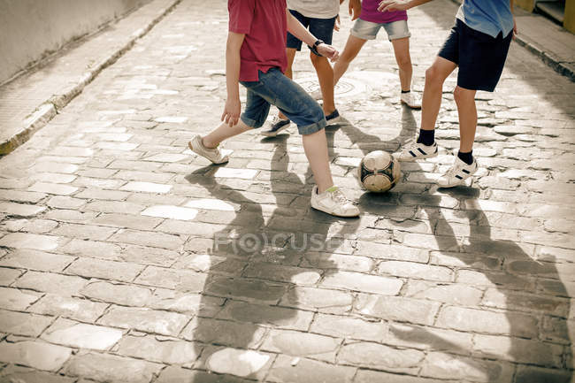 Дети играют с футбольным мячом на булыжной улице — стоковое фото