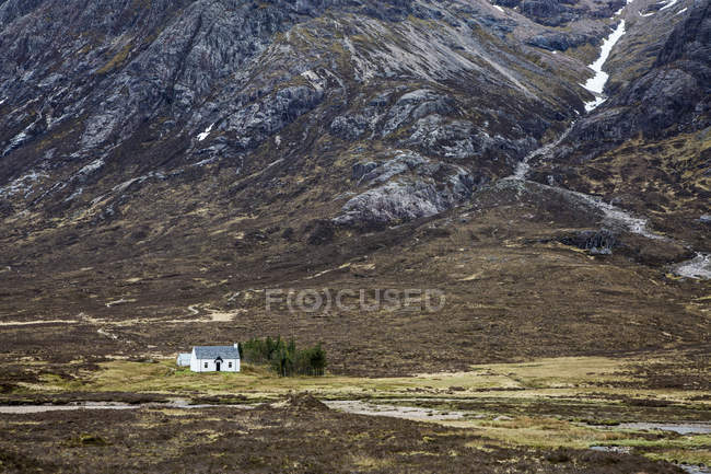 Casa en valle remoto bajo montañas escarpadas, Glencoe, Escocia - foto de stock