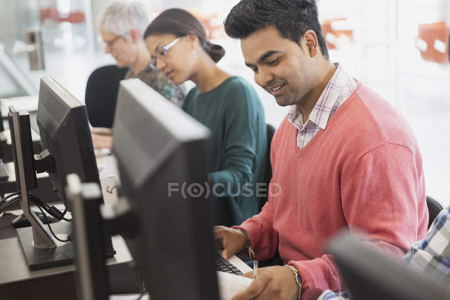 Estudiante sonriente de educación de adultos en la computadora en el aula - foto de stock