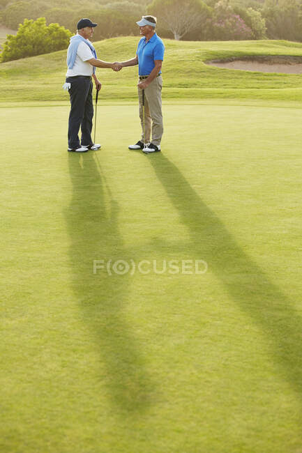 Hombres mayores estrechando la mano en el campo de golf - foto de stock