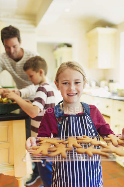 Chica sosteniendo la galleta en bandeja, padre y niño en el fondo - foto de stock