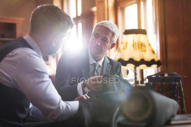 Sastre y hombre de negocios discutiendo traje en tienda de ropa masculina - foto de stock