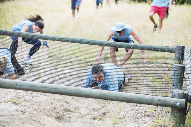 Pessoas rastejando sob a rede no campo de inicialização curso de obstáculo — Fotografia de Stock