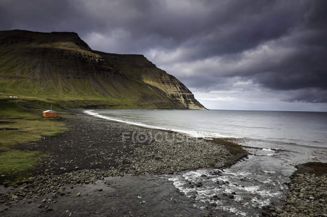 Pebble shore against water and hill on background — Stock Photo