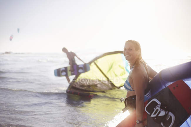 Porträt lächelnde Frau mit Kiteboard-Ausrüstung in der Brandung des Meeres — Stockfoto