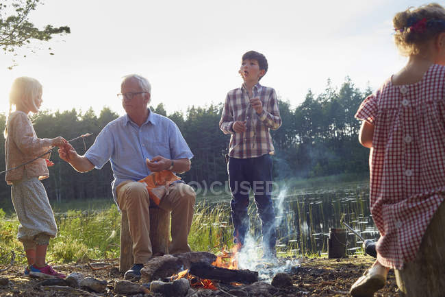 Grand-père et petits-enfants profitant du feu de camp au bord du lac — Photo de stock