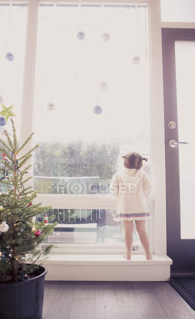 Ragazza curiosa sulla sporgenza della finestra sotto gli ornamenti di Natale — Foto stock