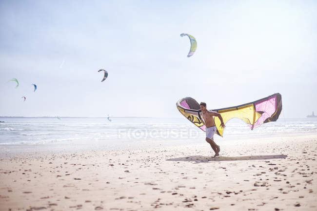 Человек, бегущий с кайтбордистом на солнечном пляже — стоковое фото