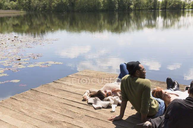 Friends laying relaxing on sunny lakeside dock — Stock Photo
