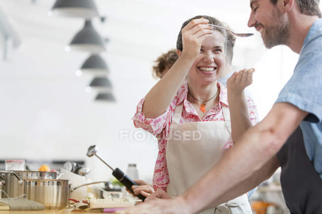 Улыбающаяся пара дегустирует еду на кухне кулинарного класса — стоковое фото