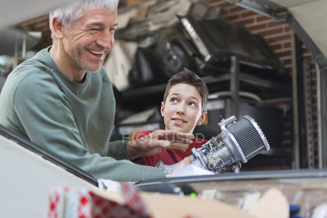 Улыбающиеся отец и сын чинят автомобильный двигатель в автомастерской — стоковое фото