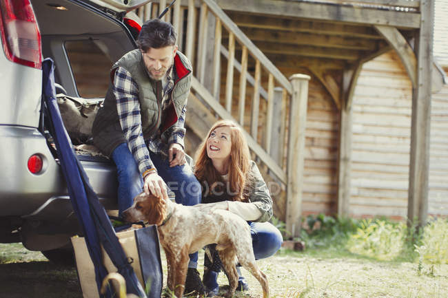 Couple with dog at back of car outside cabin — Stock Photo