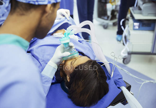 Анестезиолог держит кислородную маску на лице пациента в операционной — стоковое фото