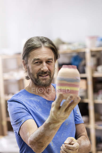 Portrait smiling mature man holding painted pottery vase in studio — Stock Photo