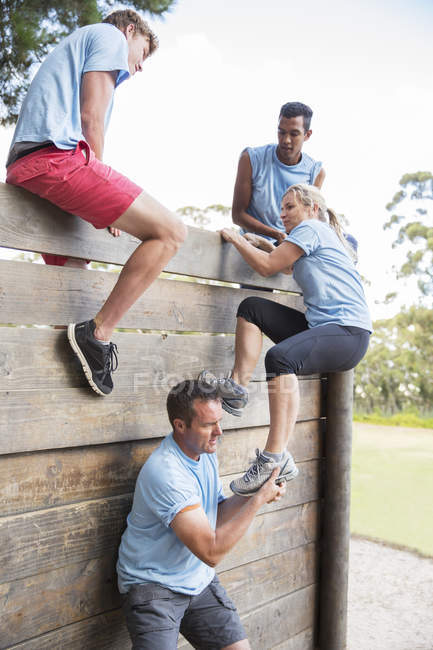 Teammates helping woman over wall on boot camp obstacle course — Stock Photo