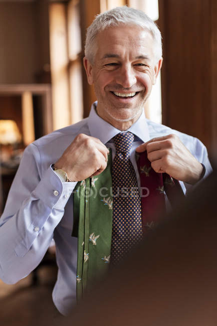 Lächelnder Geschäftsmann probiert Krawatten im Spiegel im Herrenladen an — Stockfoto