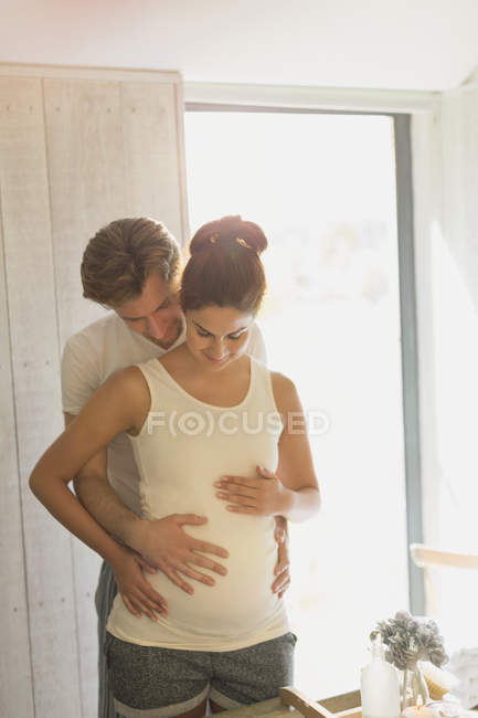 Pregnant couple holding stomach in sunny bathroom — Stock Photo
