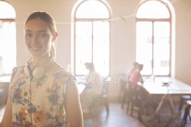 Retrato sorridente empresária casual com fones de ouvido em escritório aberto ensolarado — Fotografia de Stock