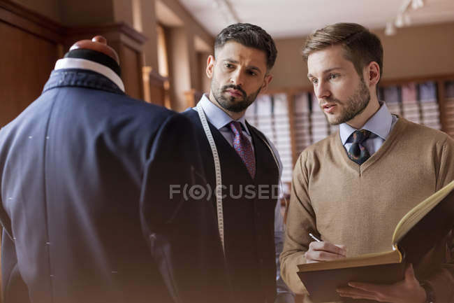 Alfaiates discutindo terno e tomar notas na loja de moda masculina — Fotografia de Stock
